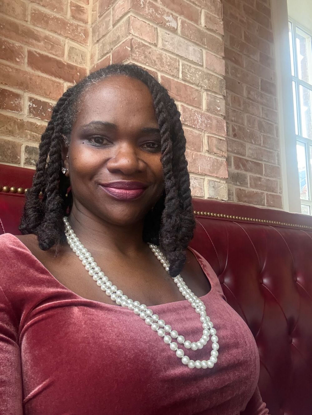 Johnnise Tisdale, founder of She Builds & Shares, smiling in a soft rose velvet top and pearl necklace