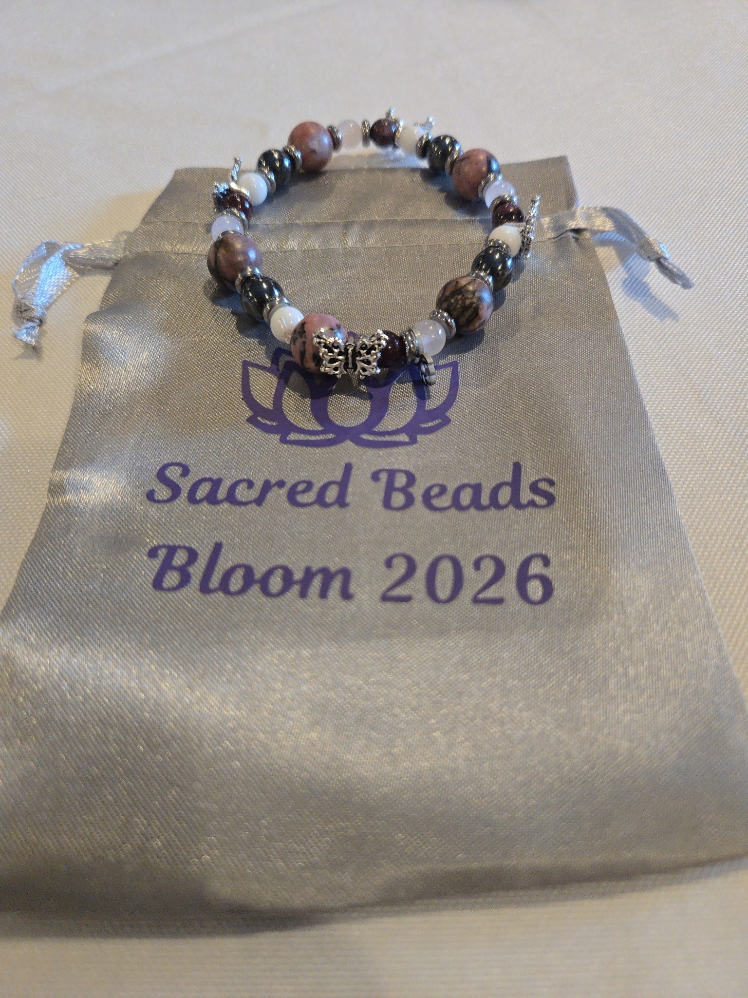 A beaded bracelet resting on a Sacred Beads Bloom 2026 keepsake pouch.
